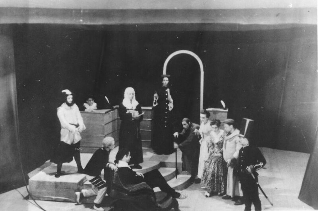 Black and white still photo of players on stages performing a scene