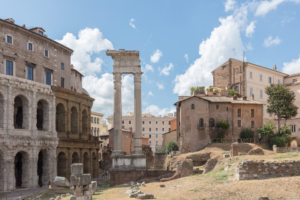 photo of the remain of the Temple of Apollo in Rome, Italy. Two standing columns in the center surrounded by scattered remains.