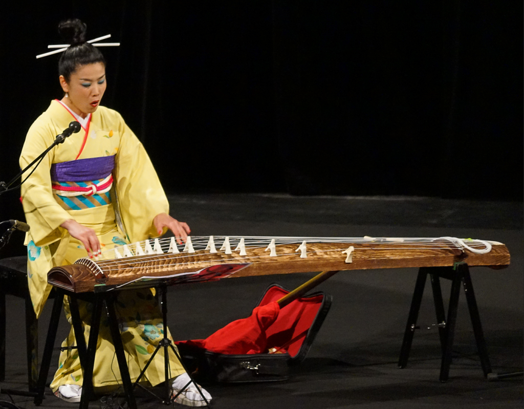 Photo of a woman dressed in a traditional japanese outfit playing the koto.