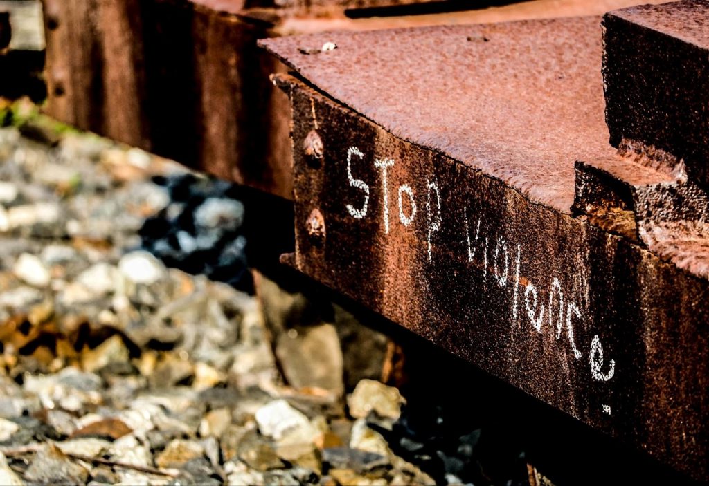 Close-up photo of corner of a rusted railroad car with "Stop violence" in white writing