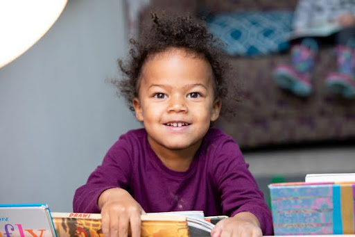 A child sits facing forward holding books.