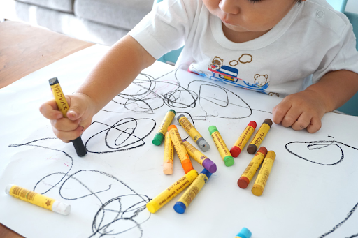 Photo of young child scribbling on paper with crayons.