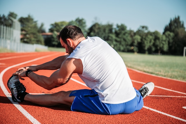 An individual completing static stretching on a track.