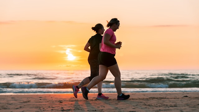 Two individuals jogging on the beach.