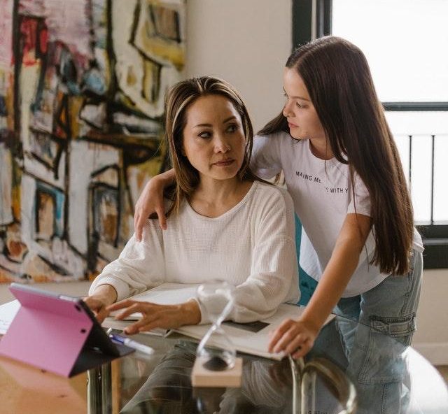 Image of a mother working on a tablet. An young adolescent child is asking the mother a question.