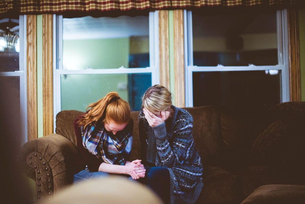 Image of an adolescent daughter holds her mother's hand. Both are crying.