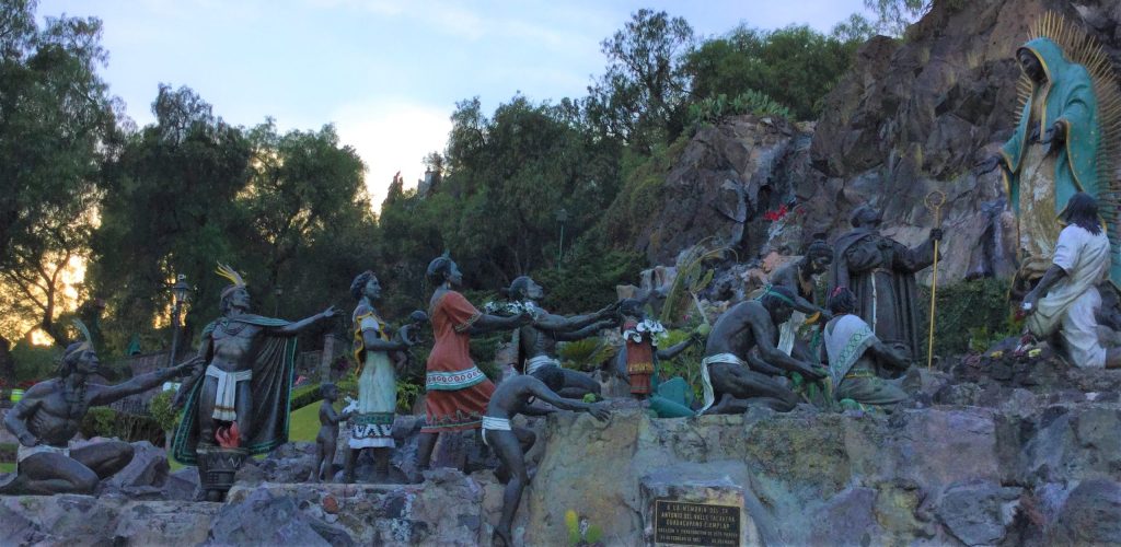 statues of indigenus people in a line reaching toward the statue of a the Virgin Mary on the far right