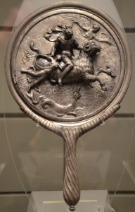 Silver hand held mirror with elaborate relief on its back.