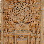 stone relief of a tree surrounded by two winged figures at the top and four figures arms in a praying position at the bottom