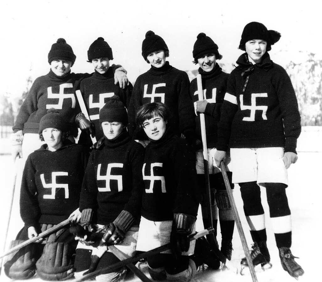 Team of female-presenting hockey players with equipment and black sweaters with white swastikas on them