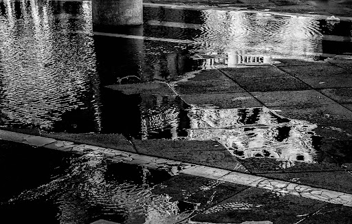 Black and white photo of water on stone ground with reflections of buildings