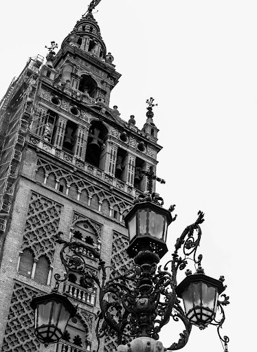 A black and white photo of a tower with decorative styling and a street lamp in front