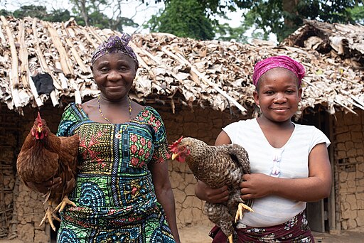 Photo of two Mbuti women carrying chickens.