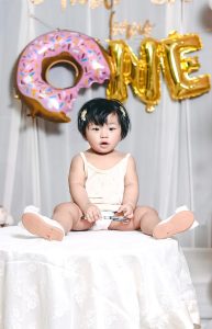 Imagen de una niña de un año sentada frente a globos que deletrean "UNO".