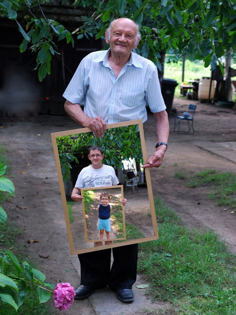 Imagen de un anciano sosteniendo una foto de su hijo sosteniendo una foto de su nieto.