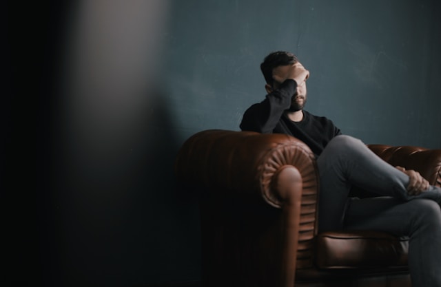 Photo of man sitting on a sofa with his right hand on his forehead.