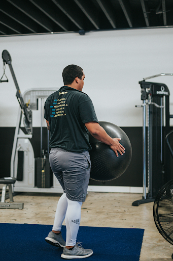 An individual in a fitness center carrying an exercise ball.